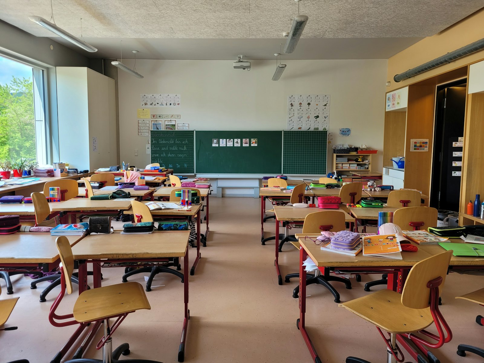 Empty primary school classroom with desks, chairs and a green chalkboard